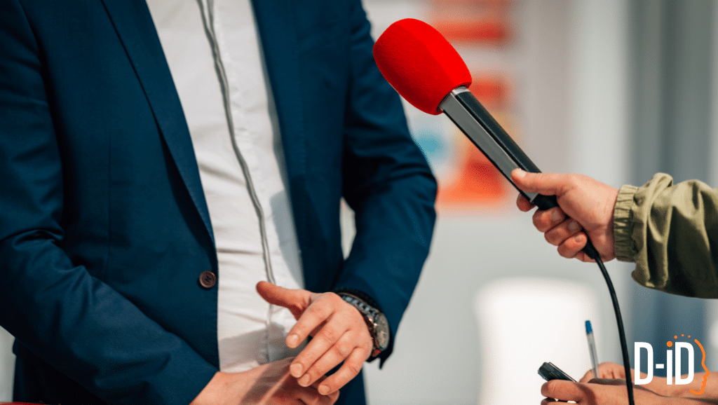A person in a suit is being interviewed, with a red microphone held near their hands by another person. The D-ID logo is visible in the bottom right corner, suggesting an AI Spokesperson may be featured using an ai spokesperson video creator.